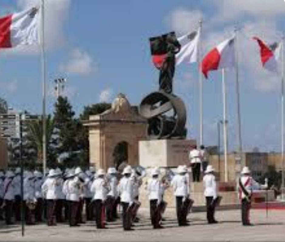 Maltese troops before a monument framed by Maltese flags at an Independence Day ceremony